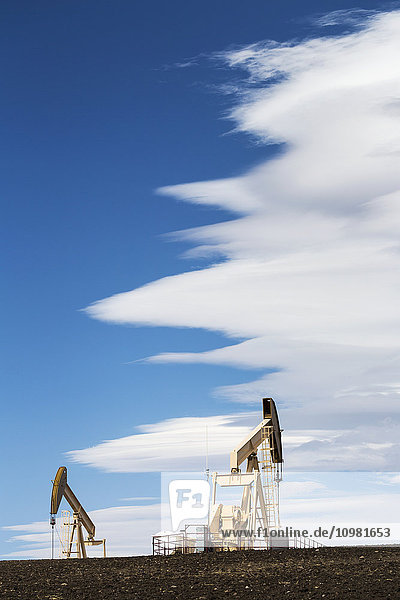 Zwei Pumpjacks auf einem Hügel mit dramatischen Wolken am blauen Himmel; Alberta  Kanada'.