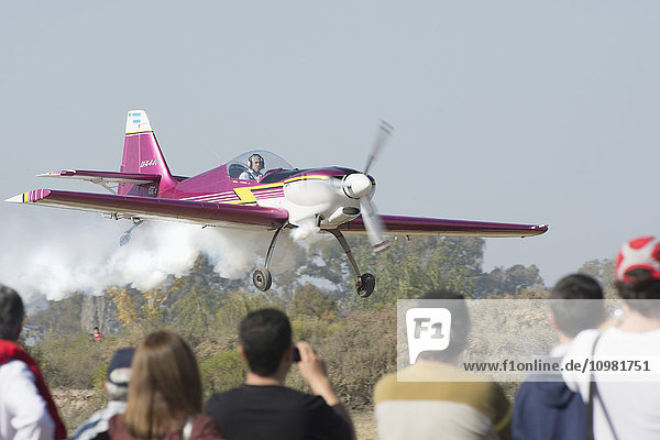 Ein Kunstflugzeug fliegt im Tiefflug mit Rauch in unmittelbarer Nähe der Zuschauer; Rivadavia  Mendoza  Argentinien'.