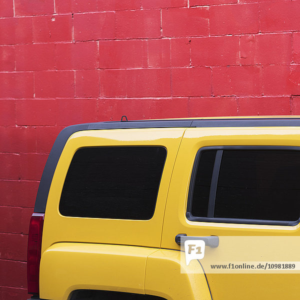 'A bright yellow vehicle parked against a painted red wall; Vancouver  British Columbia  Canada'