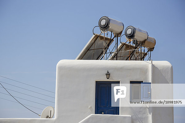 Moderne  mit Solarzellen betriebene Warmwasserbereiter zur Steigerung der Energieeffizienz sind auf dem Dach eines traditionellen griechischen Hauses montiert; Mykonos  Griechenland'.