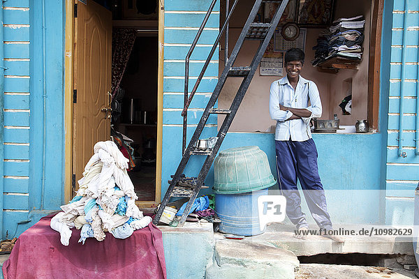 Lächelnder junger Mann vor einer kleinen gewerblichen Wäscherei; Badami  Karnataka  Indien'.