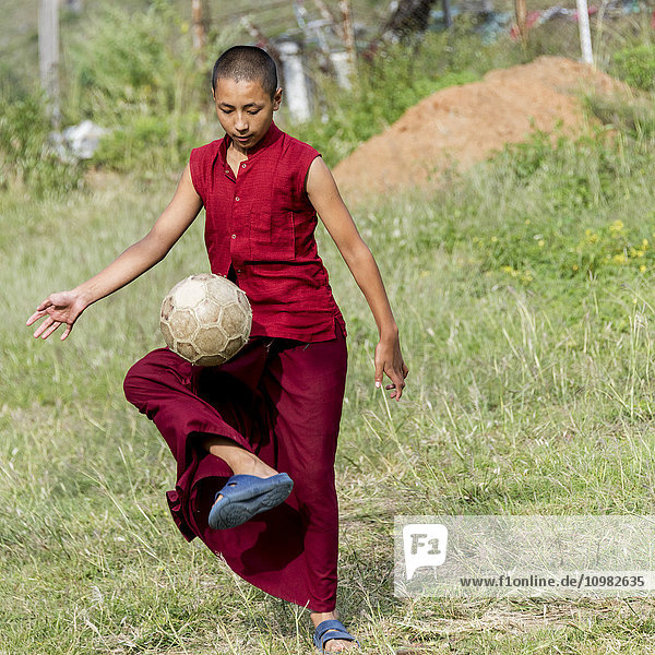 'A young monk plays with a soccer ball; Punakha  Bhutan'