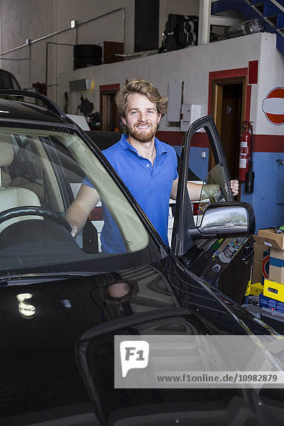 Smiling mechanic with a car in his workshop
