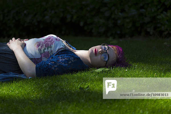 Porträt einer entspannten jungen Frau mit gefärbtem Haar auf einer Wiese liegend