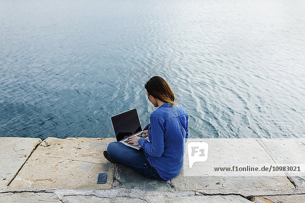 Junge Frau sitzend auf dem Dock mit Laptop