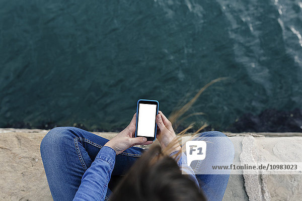 Junge Frau sitzt auf dem Dock mit dem Handy