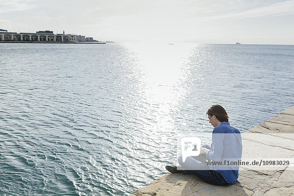 Italy  Trieste  young woman sitting on dock with a book