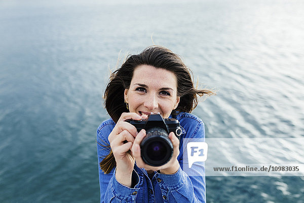 Smiling young woman at the waterfront holding camera