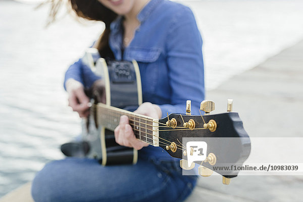Young woman at the waterfront playing guitar