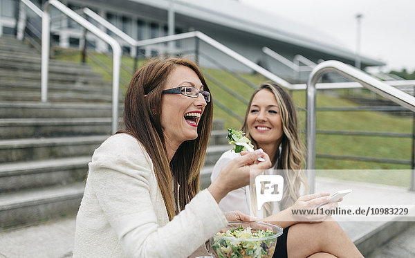 Zwei lachende Frauen beim Mittagessen im Freien