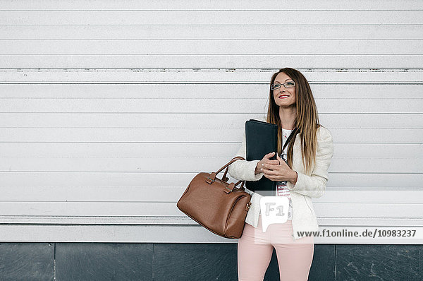Lächelnde Geschäftsfrau mit Handtasche und Mappe im Freien