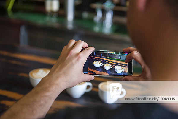 Man taking cell phone picture of cappuccino cups