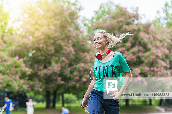 Fröhliche blonde Frau mit Kopfhörer im Park