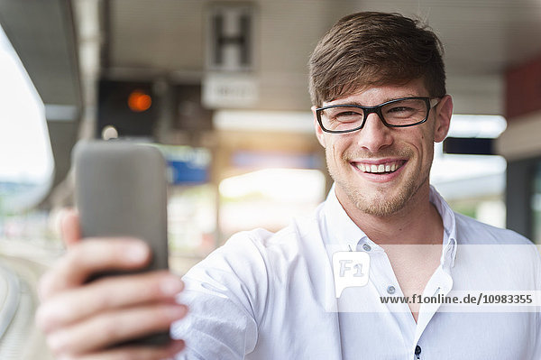 Lächelnder junger Mann am Bahnsteig mit einem Selfie