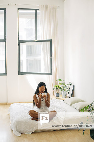 Young woman sitting on bed drinking coffee