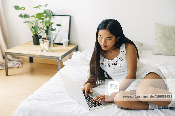 Young woman lying in bed using laptop