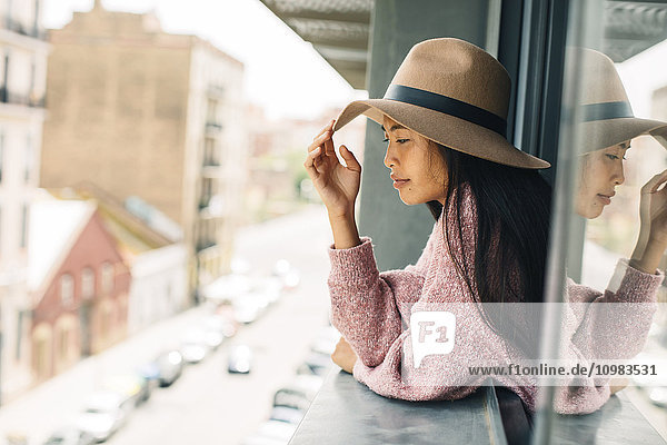 Young woman wearing hat leaning out of window