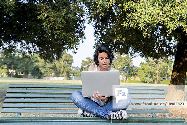 Frau sitzt auf einer Bank in einem Park mit Laptop