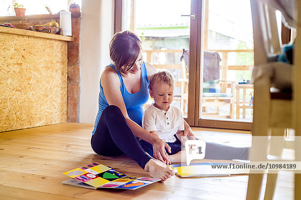 Schwangere Mutter schaut sich mit ihrem kleinen Sohn das Bilderbuch an.