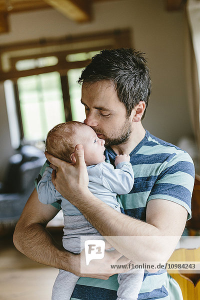 Father kissing baby boy at home