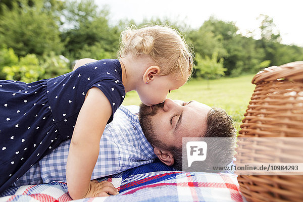 Kleines Mädchen  das seinen Vater küsst und auf einer Wiese liegt.