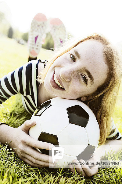 Porträt eines lächelnden Mädchens auf einer Wiese mit Kopf auf Fußball