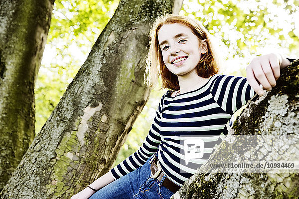 Porträt eines lächelnden Mädchens  das sich an einen Baumstamm lehnt.