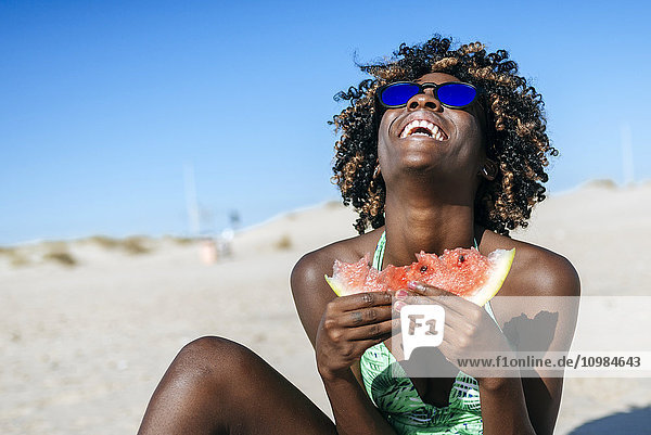 Fröhliche junge Frau isst Wassermelone am Strand