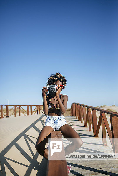 Junge Frau fotografiert auf einem Geländer am Strand sitzend