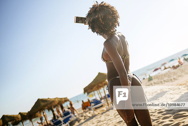 Junge Frau im Bikini mit einem Selfie am Strand