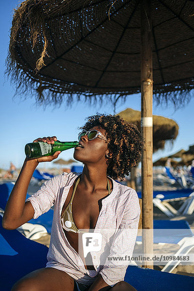 Young woman sitting on the beach drinking beer