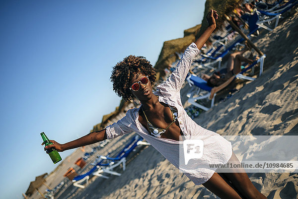 Junge Frau tanzt am Strand mit einem Bier in der Hand