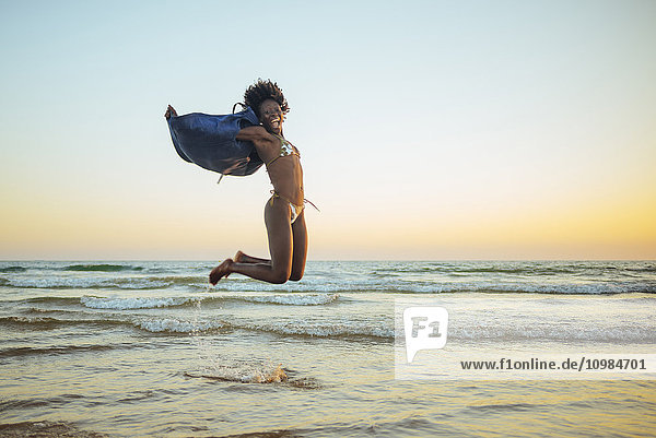 Junge Frau beim Springen am Strand bei Sonnenuntergang