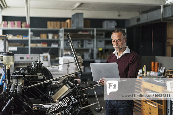 Mann in einer Druckerei mit Blick auf Laptop