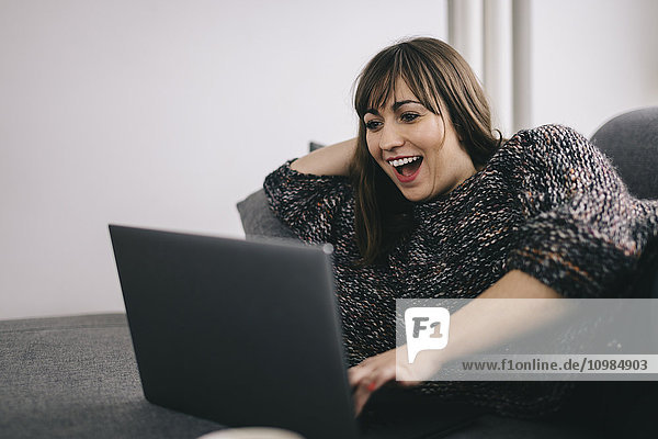 Amazed woman lying on the couch looking at laptop