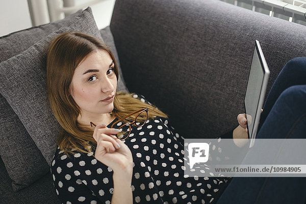 Porträt einer jungen Frau  die sich mit ihrer Tablette auf der Couch entspannt.
