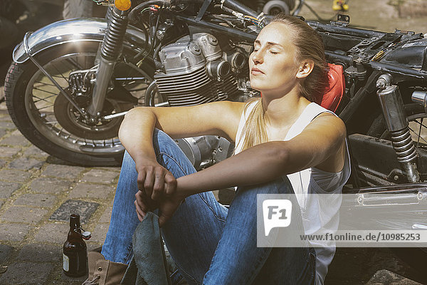 Young woman with beer bottle leaning against motorbike