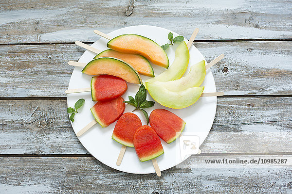 Teller mit hausgemachten Wassermelonen-Eis-Lollies,  Scheiben von Galia und Cantaloupe-Melone