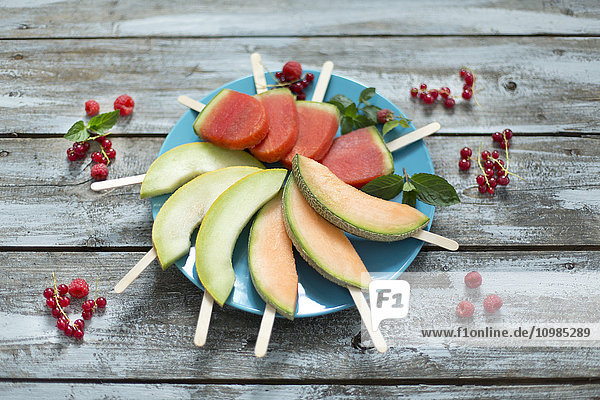 Teller mit hausgemachten Wassermelonen-Eis-Lollies,  Scheiben von Galia und Cantaloupe-Melone