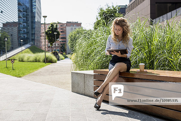 Geschäftsfrau auf der Bank sitzend mit digitalem Tablett