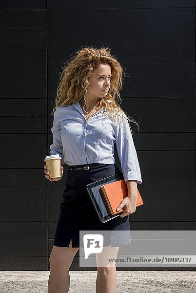 Businesswoman holding coffee to go book and digital tablet outdoors