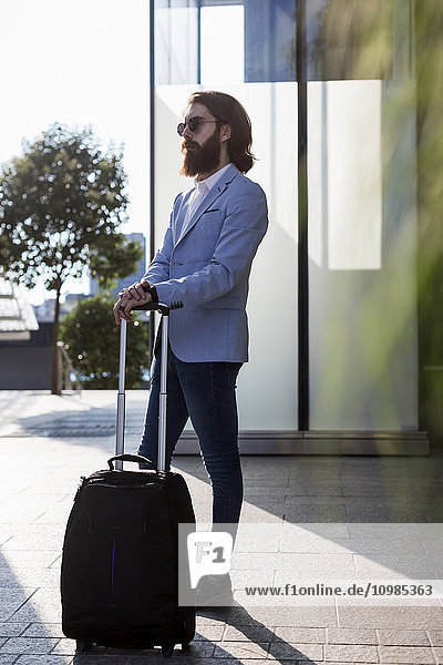 Stylish businessman walking with suitcase outdoors