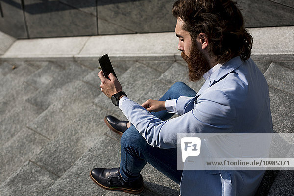 Stilvoller Geschäftsmann mit Handy auf der Treppe im Freien