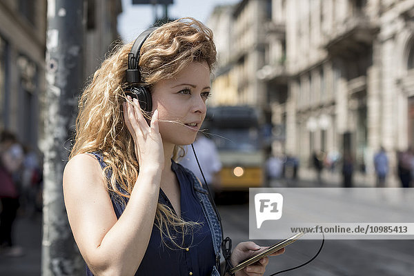 Italien  Mailand  Portrait einer jungen Frau mit Kopfhörer und Smartphone