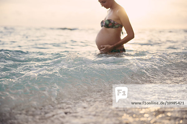 Schwangere Frau im Meer stehend bei Gegenlicht