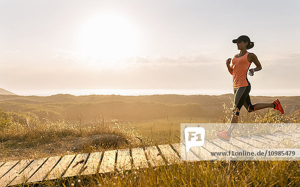 Spain  Aviles  young athlete woman running along a coastal path at sunset