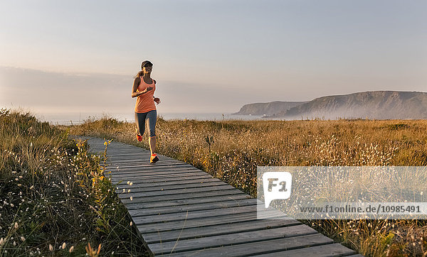 Spanien  Aviles  junge Sportlerin  die bei Sonnenuntergang einen Küstenweg entlang läuft