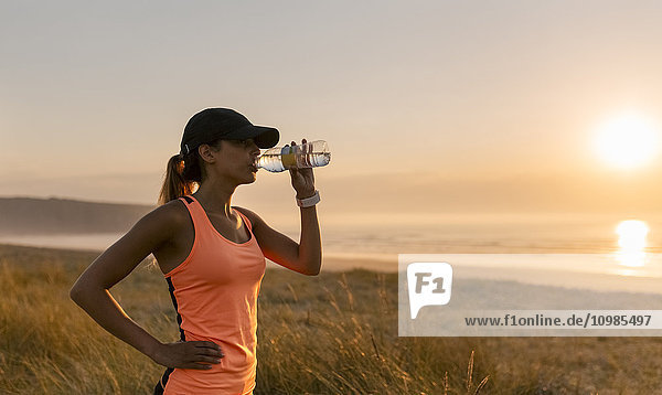 Junge Sportlerin trinkt Wasser bei Sonnenuntergang