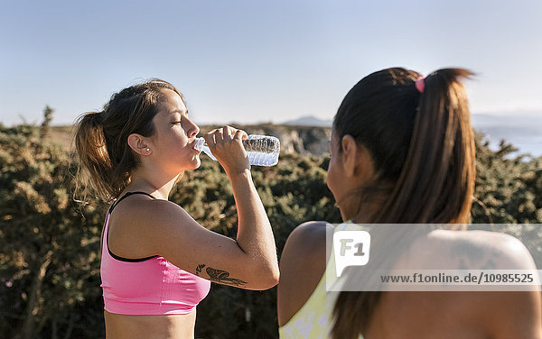 Spain  Asturias  two sportswomen training on the coast  water bottle  drinking