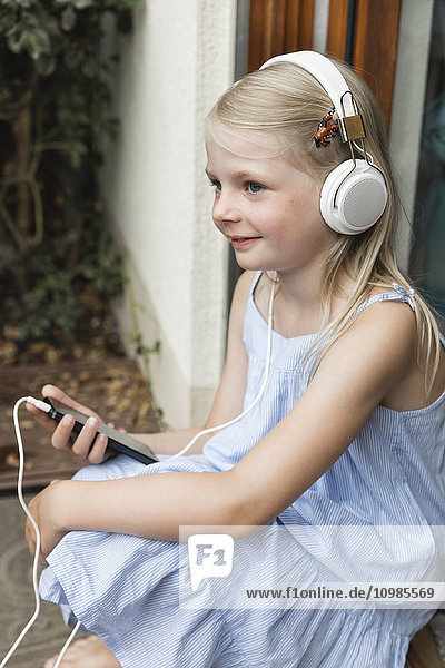 Smiling little girl listening music with headphones and smartphone